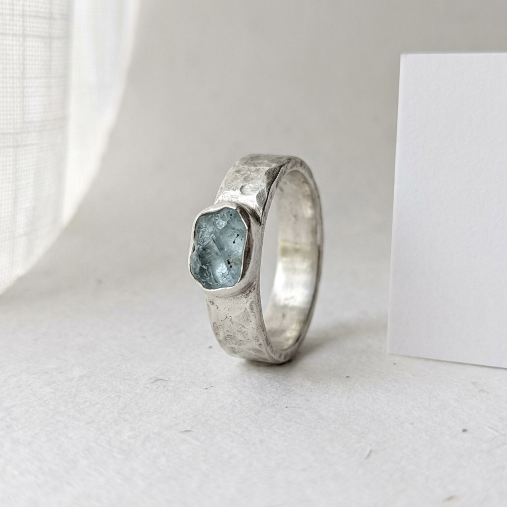 Handmade silver ring with a raw aquamarine stone lit by soft diffused daylight at a window